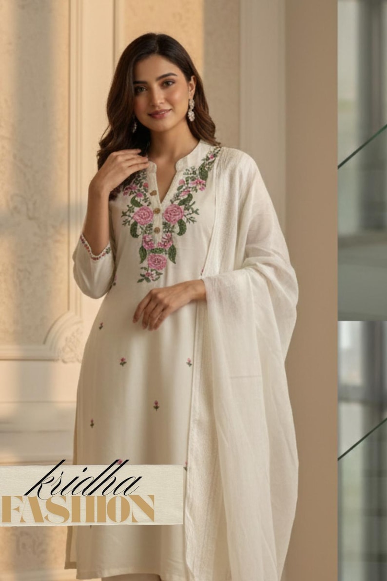 K&ouml;nnte beinhalten: Cremefarbenes besticktes Kurta-Set mit passendem Dupatta. Das Kurta hat einen Stehkragen und florale Stickereien in Rosa und Gr&uuml;n. Der Text "kridha FASHION" ist unten sichtbar.