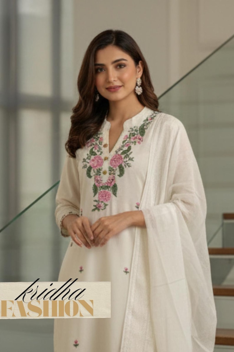 K&ouml;nnte beinhalten: Cremefarbener bestickter Kurta-Anzug mit passendem Dupatta. Der Kurta hat ein florales Design in Rosa und Gr&uuml;n um den Halsausschnitt. Der Text "kridha FASHION" ist auf dem Kleidungsst&uuml;ck zu sehen.