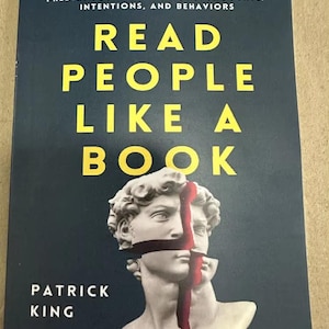 May include: A book titled "Read People Like a Book" with a dark blue cover. The title is in large yellow letters. The cover features a white statue with a red vertical line and cross. The author's name, Patrick King, is at the bottom.