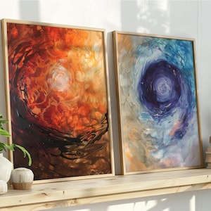 May include: Two framed abstract paintings. One features swirling orange, red, and brown hues with a central light area. The other displays a blue and white vortex design. Both are in light wood frames.