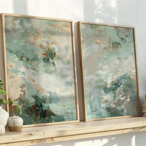 May include: Two framed abstract art prints with a light wood frame. The artwork features a blend of green, beige, and white brushstrokes. The prints are displayed on a wooden shelf with decorative items and plants.