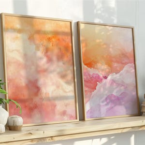 以下が含まれることがあります： オレンジ、ピンク、紫の色合いの水彩画風のデザインが施された、額装された2つの抽象芸術プリント。 木製の棚に飾られたアートワークは、装飾品や植物とともに、穏やかで芸術的な雰囲気を醸し出しています。