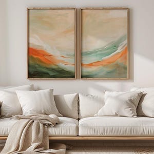 May include: A living room with a light-coloured sofa, white cushions, and a beige throw. Two framed abstract paintings in orange, green, and beige tones are above the sofa. A vase of dried flowers sits on a side table, creating a warm atmosphere.
