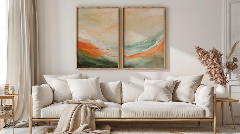 May include: A living room with a light-coloured sofa, white cushions, and a beige throw. Two framed abstract paintings in orange, green, and beige tones are above the sofa. A vase of dried flowers sits on a side table, creating a warm atmosphere.