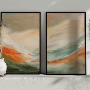 May include: Two framed abstract art prints with black frames. The artwork features flowing layers of orange, green, and beige colours. Decorative pampas grass is in white vases on either side of the art.