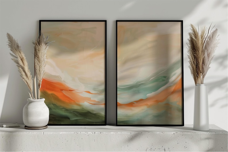 May include: Two framed abstract art prints with black frames. The artwork features flowing layers of orange, green, and beige colours. Decorative pampas grass is in white vases on either side of the art.