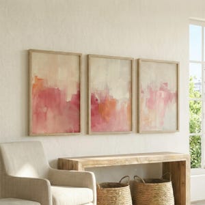 Puede incluir: Un conjunto de tres cuadros rectangulares con pinceladas abstractas en tonos crema, rosa suave y coral. Cada pieza está encerrada en un marco de madera de tono claro y fino, mostrando una aplicación de pintura texturizada y en capas.