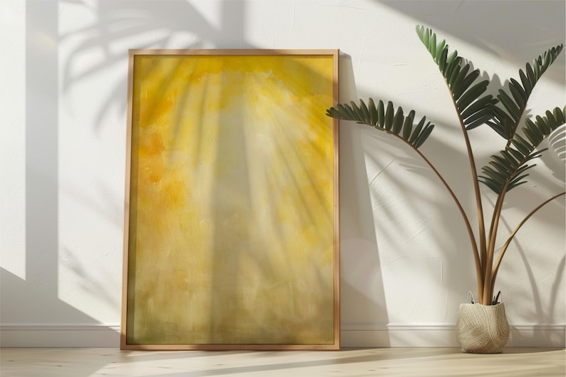 Pode incluir: Uma obra de arte abstrata emoldurada com uma paleta de cores amarelas e douradas, encostada a uma parede branca. A obra de arte tem uma apar&ecirc;ncia suave e desfocada, com efeitos de luz e sombra. Uma planta em vaso com folhas verdes est&aacute; &agrave; direita.