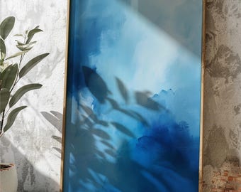 May include: Abstract art print in a wooden frame. The artwork features shades of blue, creating a sense of depth and movement. The shadow of a plant falls across the artwork. The frame is a light brown color.