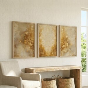 May include: Three framed abstract artworks in neutral tones. The art pieces feature beige, brown, and gold hues, creating a textured effect. The light wood frames complement the warm colours of the artwork. The frames are a light wood colour.