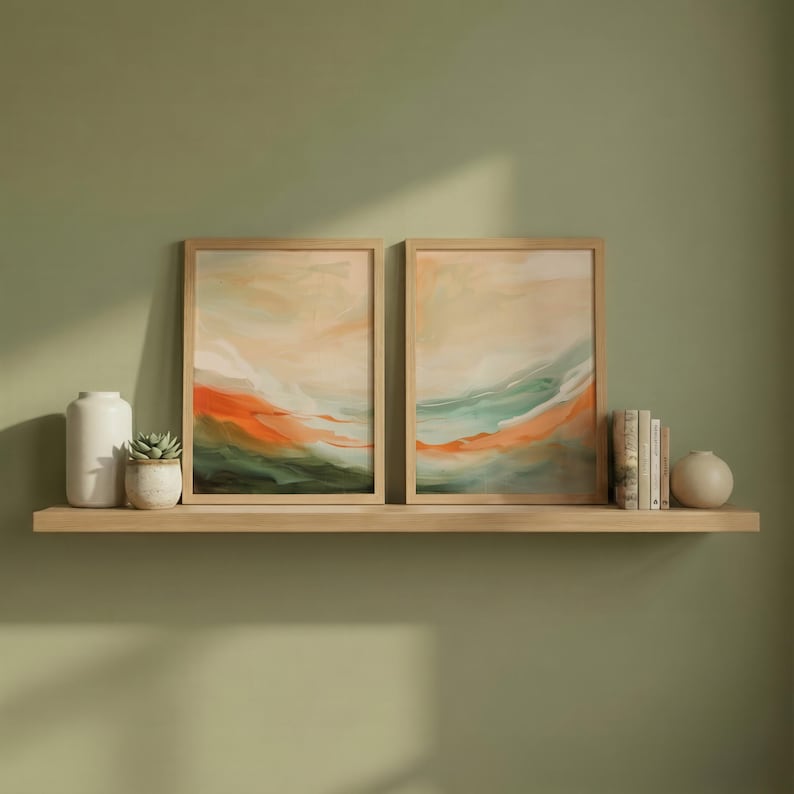 May include: Two framed abstract landscape paintings with orange, green, and beige tones. The artwork is displayed on a light wood shelf, with a white vase, a small succulent in a pot, books, and a small spherical vase.