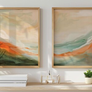 May include: Two framed abstract art prints. Each features a landscape design with orange, green, and beige hues. The artwork is displayed on a light-coloured wooden shelf with plants and decorative items.