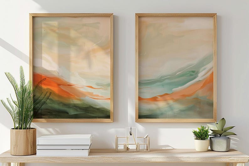 May include: Two framed abstract art prints. Each features a landscape design with orange, green, and beige hues. The artwork is displayed on a light-coloured wooden shelf with plants and decorative items.