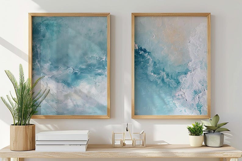 May include: Two framed abstract art prints with a light wood frame. The artwork features shades of blue and white, resembling ocean waves. The prints are displayed above a wooden shelf with plants and books.