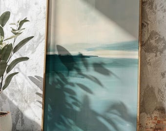 May include: Abstract landscape art print in a wooden frame. The artwork features a serene scene with shades of teal, blue, and cream. The frame is a light brown color. The image is leaning against a textured wall.