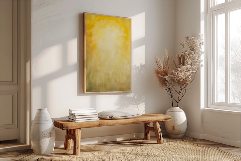 Pode incluir: Uma cena interior acolhedora com um banco de madeira, livros e uma almofada. Uma grande pintura abstrata em tons de amarelo e verde est&aacute; pendurada na parede. Um vaso com flores secas e um vaso branco grande completam a decora&ccedil;&atilde;o.