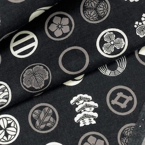 May include: Dark fabric featuring a repeating pattern of white and grey circular designs. The circles contain various stylized floral and geometric motifs. The fabric is folded, showing the pattern at different angles.