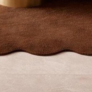 Luxury solid brown area rug with soft wavy edges placed in a modern minimalist living space, contemporary carpet on marble floor with wooden table and neutral walls, elegant modern rug for living room bedroom and hallway décor
