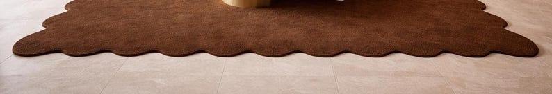 Luxury solid brown area rug with soft wavy edges placed in a modern minimalist living space, contemporary carpet on marble floor with wooden table and neutral walls, elegant modern rug for living room bedroom and hallway décor