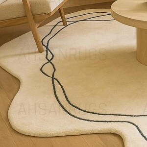 Modern irregular shaped cream rug with abstract wavy edge design, minimalist black and orange line art pattern, contemporary carpet for living room or bedroom décor.