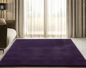 May include: A rectangular, deep purple rug. The rug is placed on a light-colored floor in front of a large window with sheer white curtains. The rug's texture appears soft and plush, adding warmth to the room.