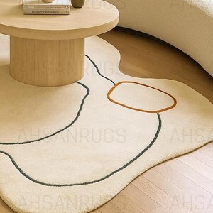 Modern irregular shaped cream rug with abstract wavy edge design, minimalist black and orange line art pattern, contemporary carpet for living room or bedroom décor.