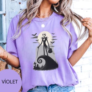 May include: Violet t-shirt with a black and white illustration of Jack Skellington from The Nightmare Before Christmas. The design includes a full moon, bats, and a swirling hill. The word "VIOLET" is printed on a purple circle.