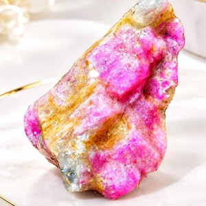 May include: A raw, unpolished mineral specimen featuring vibrant magenta and pink crystalline structures contrasted with streaks of earthy tan and translucent white quartz, showcasing a jagged, natural texture with irregular facets.