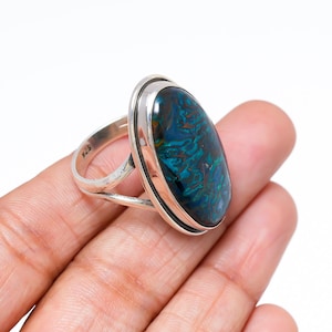 May include: A silver ring with a large, oval gemstone displaying a swirling pattern of blue and green. The ring has a simple, polished design. The gemstone's colours create a striking contrast against the silver setting.
