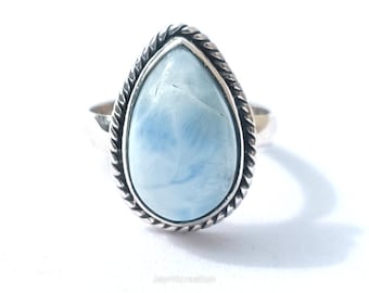 May include: A silver ring featuring a pear-shaped, light blue gemstone. The stone is set in a silver bezel with a twisted rope design. The ring is displayed on a white background, highlighting the jewelry.