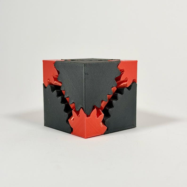 May include: A geometric puzzle cube constructed from interlocking matte black and vibrant red plastic components. The design features jagged, saw-toothed edges where the two colors meet, creating a complex, multi-layered structural appearance.