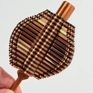 May include: A handheld object featuring a series of alternating copper-colored and black horizontal discs stacked to form a rounded, ribbed shape. A smooth copper-colored cylindrical post extends from the top, and a textured brown handle extends from the bottom.