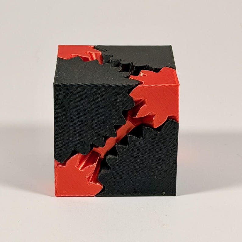 May include: A 3D printed mechanical cube puzzle featuring interlocking black and red gear components. The object is constructed from solid geometric sections that fit together with jagged, tooth-like edges, creating a complex, multi-part assembly.