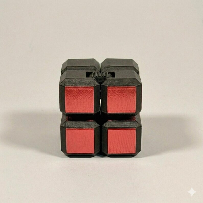 May include: A black and red fidget cube puzzle toy composed of eight smaller connected blocks. The structure features a matte black frame with metallic red square panels on the front faces, showing a grid of four distinct red squares.