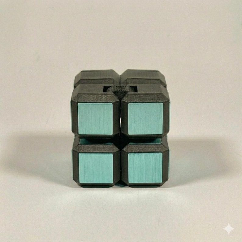 May include: A black fidget cube puzzle with a matte finish and metallic light blue square inlays on each face. The cube features a textured surface and a small black gear wheel visible between the top two segments of the puzzle structure.