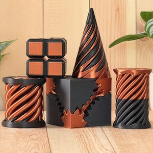 May include: A collection of five geometric objects in matte black and metallic copper. The set includes a four-part cube, a tall cone with spiral grooves, a central cube with interlocking gear-like edges, and two cylindrical spools with spiral patterns.