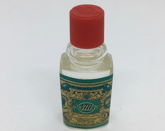 May include: A small, clear glass bottle of 4711 Echt Kölnisch Wasser cologne with a red cap. The label features teal and gold ornate designs and text. The bottle is rectangular with rounded edges.