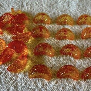Puede incluir: Rodajas y segmentos de fruta de resina translúcida naranja y amarilla. Las piezas están dispuestas sobre una superficie blanca texturizada. Los segmentos tienen forma de semicírculo y las rodajas tienen varias formas.