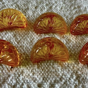 Pode incluir: Seis contas de vidro translúcidas, laranja-amarelas, em forma de semicírculo, com um design texturizado em forma de leque. As contas estão dispostas sobre uma superfície branca e texturizada. As contas têm um centro vermelho-alaranjado.