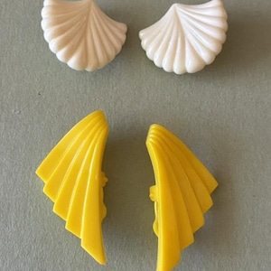 Pode incluir: Um par de brincos brancos em forma de concha com textura canelada e um par de brincos amarelos em forma de leque com um design angular escalonado. Estes quatro brincos individuais apresentam um acabamento liso, brilhante e formas geométricas.