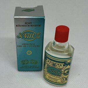 Pode incluir: Uma pequena garrafa de Eau de Cologne com tampa vermelha e caixa a condizer. A caixa e a garrafa apresentam o texto "Echt Kölnisch Wasser" e "4711" num design turquesa e dourado. A garrafa é transparente e o líquido é visível.