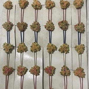Pode incluir: Uma exibição de broches florais vintage. Cada broche apresenta um grupo de pequenas rosas detalhadas em tons de amarelo, rosa e verde. Os broches estão presos a um cartão com o texto "NEW FORM" no topo.