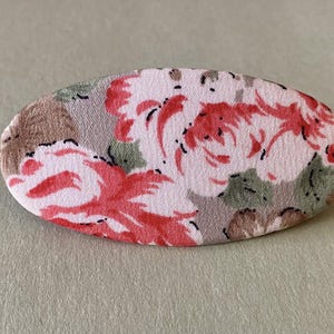 Può includere: Fermaglio per capelli ovale in tessuto con motivo floreale. La clip presenta rose rosse e foglie verdi su sfondo grigio chiaro e marrone. Un accessorio per capelli decorativo.