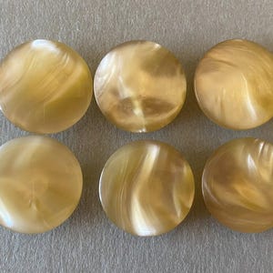 Può includere: Sei bottoni rotondi vintage con un motivo perlato e vorticoso nei toni crema e oro. I bottoni sono disposti in due file da tre, mettendo in risalto la loro superficie lucida e lucidata. Questi bottoni sono ideali per cucito e progetti artigianali.