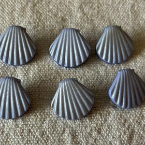 May include: Six small, pearlescent grey seashell-shaped decorative items. Each shell has a ridged texture and a curved shape, arranged on a neutral-coloured fabric surface. Suitable for crafts or home decor.