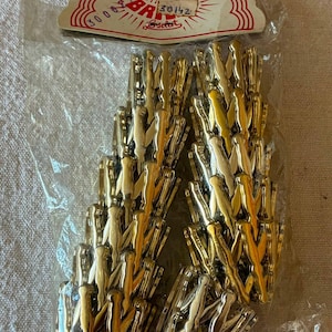 May include: A package of gold-toned metal clothespins in a clear plastic bag with a cardboard header. The header features red text reading "BR" and "30142" on a white background. The clothespins are arranged in two vertical columns inside the bag.