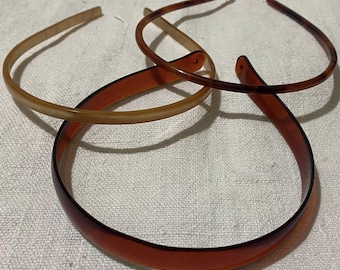 Puede incluir: Tres diademas de plástico en tonos marrón y beige están dispuestas sobre una superficie texturizada blanquecina. Las diademas varían en anchura y color, con un estampado carey visible en dos de ellas. Accesorios para el cabello sencillos y elegantes.