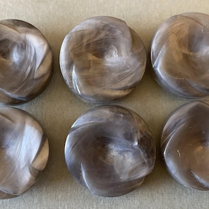 Puede incluir: Seis botones redondos con un patrón de remolino en tonos grises y blancos. Los botones tienen un acabado brillante y una forma ligeramente abovedada. Estos botones decorativos son adecuados para proyectos de costura y artesanía.