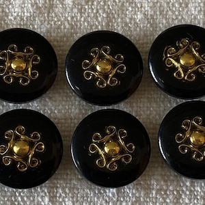 Può includere: Dieci bottoni neri con un design a filigrana dorata. Ogni bottone ha una finitura lucida e un centro dorato in rilievo. I bottoni sono rotondi e ben distanziati, per cucito o artigianato.