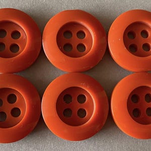 May include: Six orange buttons with four holes each. The buttons are round with a slightly raised edge and a glossy finish. These buttons are suitable for sewing projects.